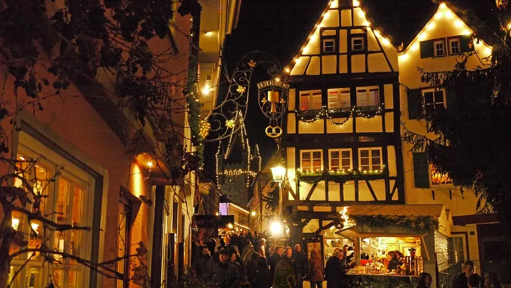 Illuminated half-timbered houses, a market stall and visitors in the evening, the Blauer Turm in the background