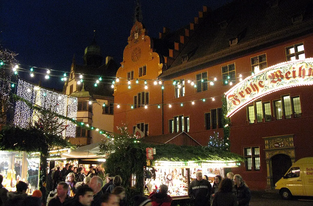 Stalls on Rathausplatz in the evening, behind them the New and Old Town Halls with fairy lights