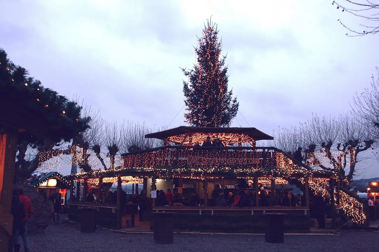 Illuminated mulled wine hut with a Christmas tree on the lakeshore at dusk