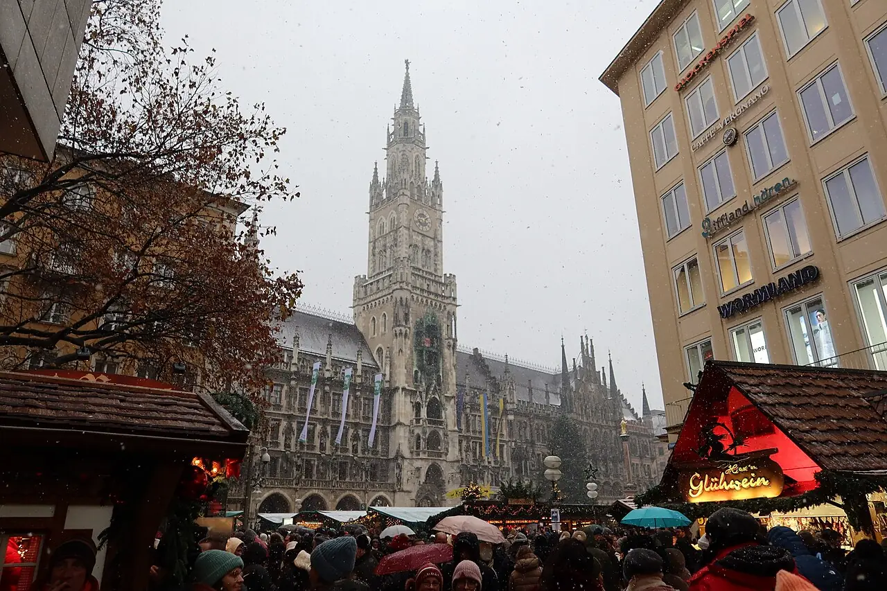 Market stalls and visitors in falling snow, with the tower of the New Town Hall behind
