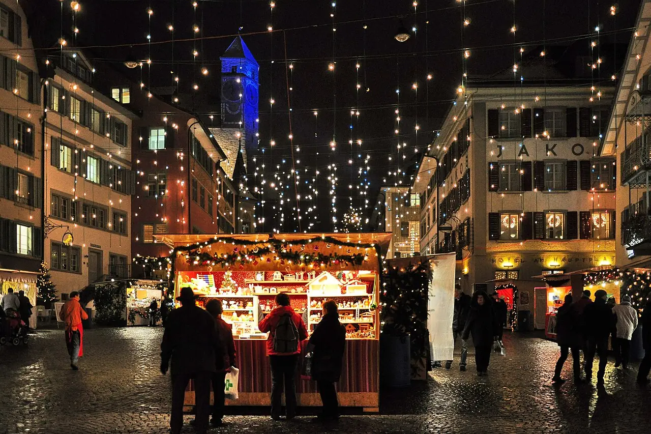 Illuminated stall with wooden toys on Hauptplatz at night, with the castle tower behind it (2010)