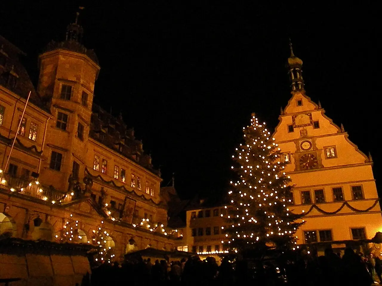 Town hall and Ratstrinkstube with an illuminated Christmas tree and market stalls in the evening