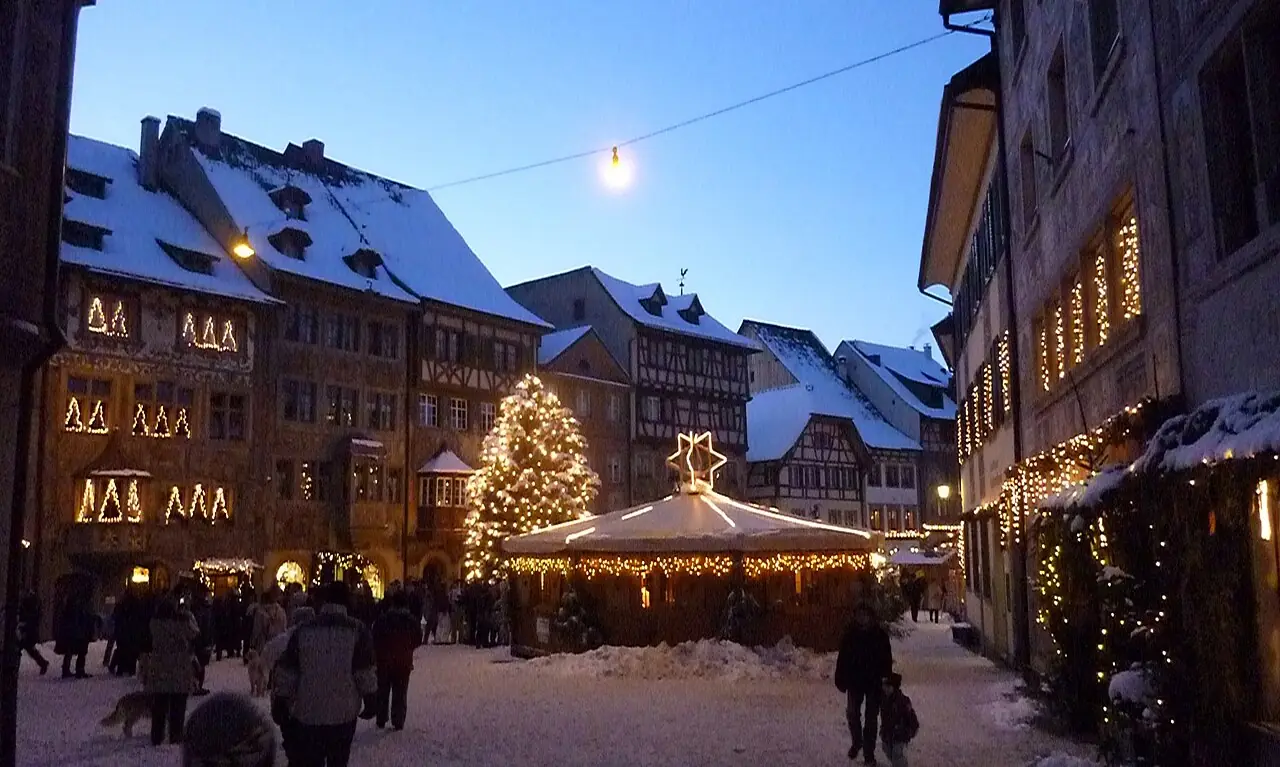 Snow-covered Rathausplatz at dusk with an illuminated carousel, Christmas tree and lights on the façades (2010)