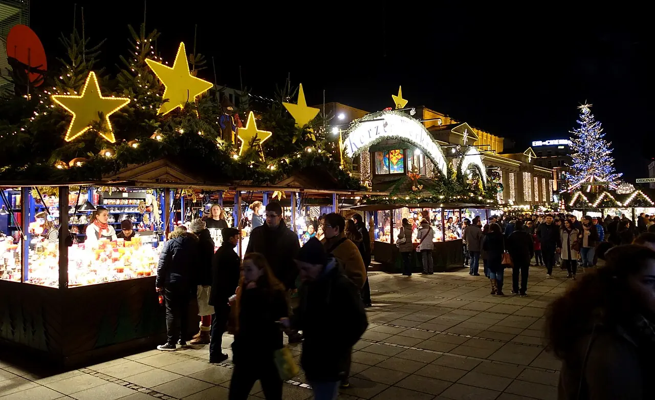 Stalls with illuminated stars and fir greenery on the roofs in the evening, an illuminated Christmas tree in the background