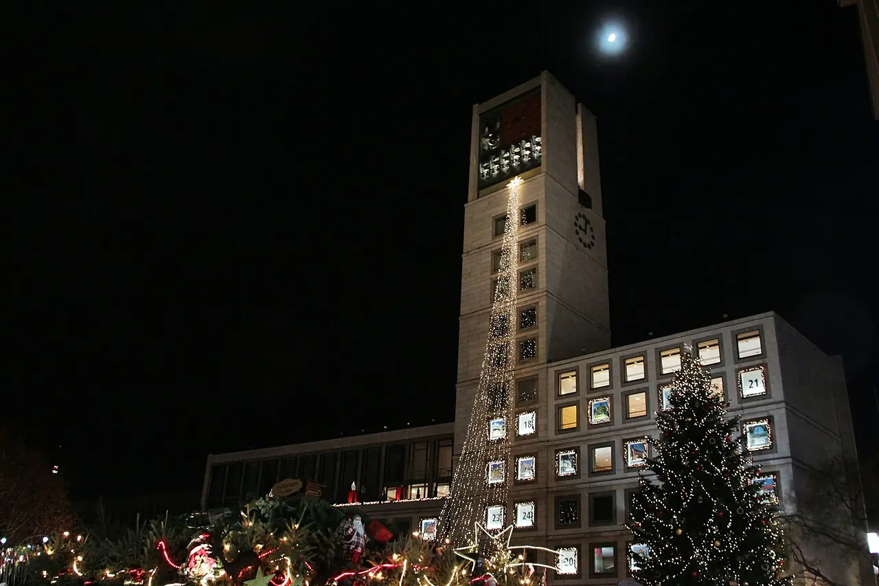 Town hall with Advent calendar windows and a string of lights at night, decorated stall roofs on Marktplatz in front