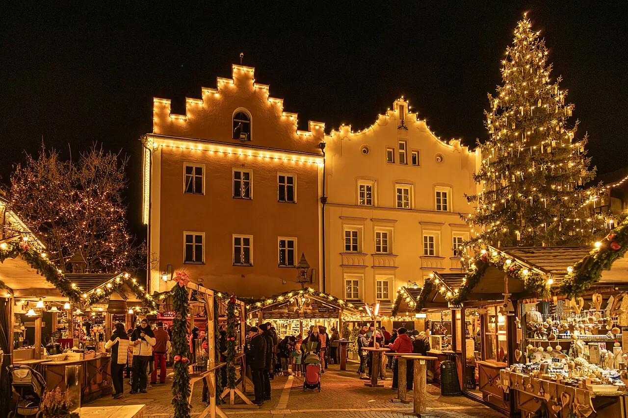 Sterzinger Glockenweihnacht at night: huts, visitors, a big Christmas tree in front of illuminated houses with stepped gables