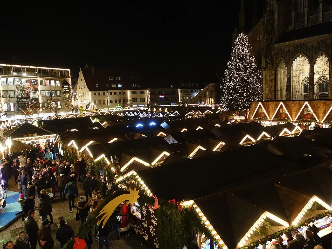Illuminated stall roofs on Münsterplatz at night, the Christmas tree on the right in front of the Minster portal