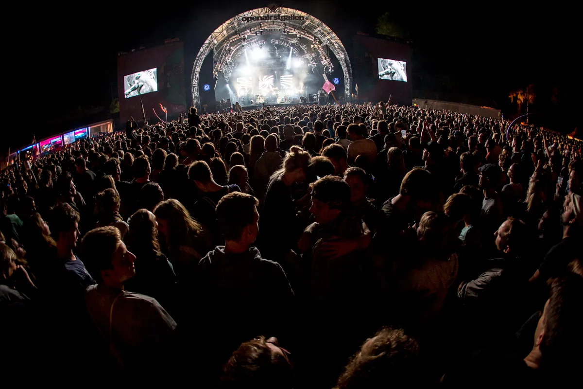 Publikum bei Nacht vor der beleuchteten Hauptbühne des OpenAir St.Gallen im Sittertobel